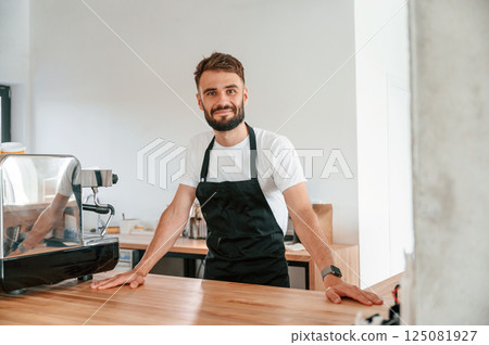 Cafe worker in white shirt and black apron is indoors Cafe worker in white shirt and black apron is indoors 125081927