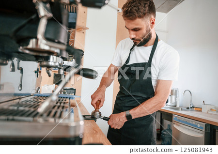 Using coffee machine. Cafe worker in white shirt and black apron is indoors 125081943