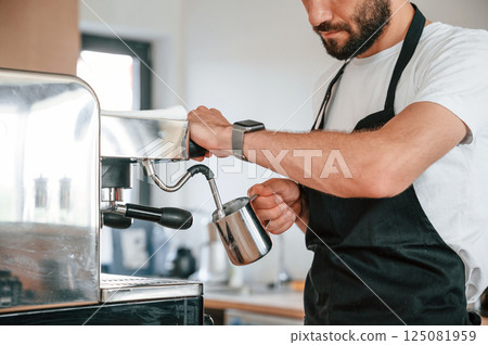 Standing and pouring coffee. Cafe worker in white shirt and black apron is indoors 125081959
