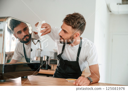 Cleaning coffee machine. Cafe worker in white shirt and black apron is indoors 125081976