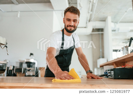 Cleaning table. Cafe worker in white shirt and black apron is indoors 125081977