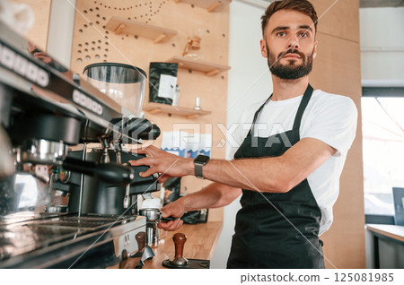 Preparing the coffee machine. Cafe worker in white shirt and black apron is indoors 125081985