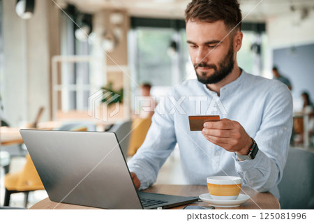 Making payment by credit card. Young man is sitting in the cafe and working by using laptop 125081996