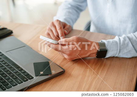 Credit card is on the laptop. Close up view of man that sitting by the table and working by using smartphone 125082003