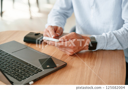 Credit card is on the laptop. Close up view of man that sitting by the table and working by using smartphone Credit card is on the laptop. Close up view of man that sitting by the table and working by using smartphone 125082004