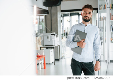 With laptop in hand. Young office worker in formal clothes is indoors With laptop in hand. Young office worker in formal clothes is indoors 125082008