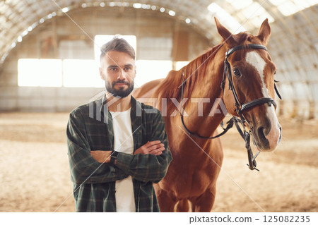 Young man with a horse is in the hangar 125082235
