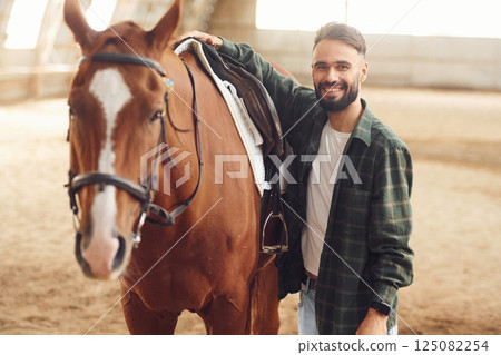 Installing the saddle. Young man with a horse is in the hangar 125082254