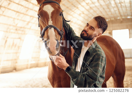 Standing together. Young man with a horse is in the hangar 125082276