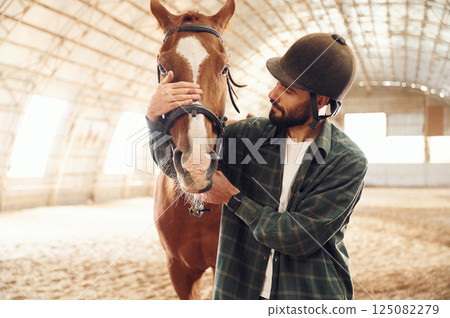 Front view. Young man with a horse is in the hangar Front view. Young man with a horse is in the hangar 125082279