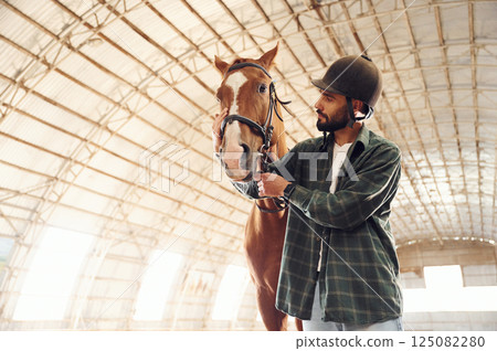 Front view. Young man with a horse is in the hangar Front view. Young man with a horse is in the hangar 125082280