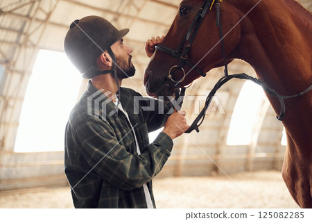 Taking care of animal. Young man with a horse is in the hangar Taking care of animal. Young man with a horse is in the hangar 125082285
