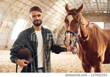 Positive emotions. Front view. Young man with a horse is in the hangar 125082291
