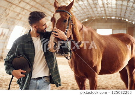 Positive emotions. Front view. Young man with a horse is in the hangar 125082293