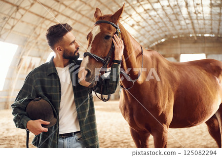 Positive emotions. Front view. Young man with a horse is in the hangar 125082294
