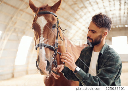 Close up view. Touching the animal. Young man with a horse is in the hangar 125082301