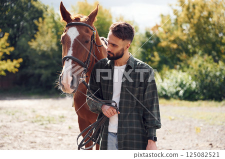 Front view. Young man with a horse is outdoors 125082521