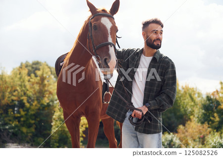 In casual clothes. Young man with a horse is outdoors 125082526