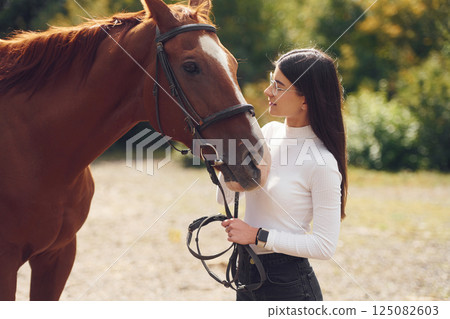 Touching the animal. Young beautiful woman with a horse is outdoors Touching the animal. Young beautiful woman with a horse is outdoors 125082603