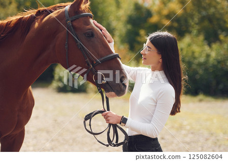 Touching the animal. Young beautiful woman with a horse is outdoors Touching the animal. Young beautiful woman with a horse is outdoors 125082604