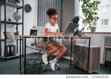 Using laptop. Cute female african american student child is sitting by the table Using laptop. Cute female african american student child is sitting by the table 125082639