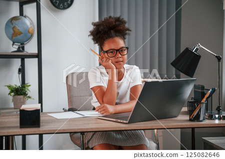 Cute female african american student child is sitting by the laptop Cute female african american student child is sitting by the laptop 125082646