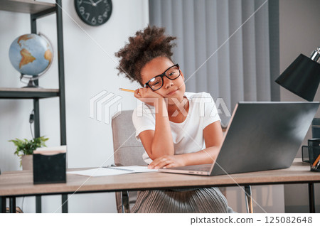 With pen. Cute female african american student child is sitting by the laptop 125082648