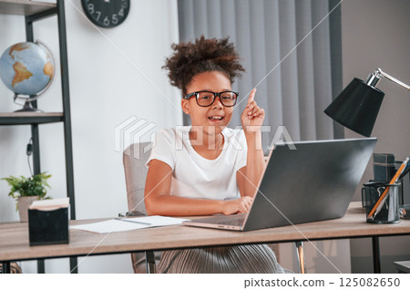 Have an idea, raises finger up. Cute female african american student child is sitting by the laptop Have an idea, raises finger up. Cute female african american student child is sitting by the laptop 125082650