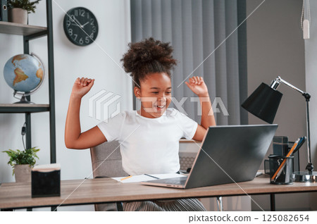 Celebrating success. Passes the exam. Cute female african american student child is sitting by the laptop 125082654