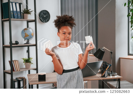 Holding paper stickers. Cute african american child is standing in the domestic room Holding paper stickers. Cute african american child is standing in the domestic room 125082663
