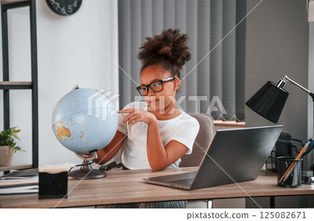 Examining the globe. Cute female african american student child is sitting by the laptop 125082671