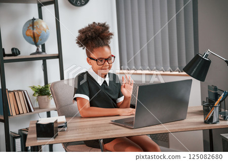 Sitting by the table with laptop. Cute female african american student child 125082680