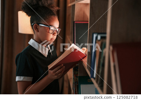 With book in hand. Beautiful light. Cute african american girl in school uniform is at home library With book in hand. Beautiful light. Cute african american girl in school uniform is at home library 125082718