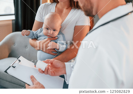 With a prescription. Male doctor is taking care of woman's newborn baby indoors With a prescription. Male doctor is taking care of woman's newborn baby indoors 125082829