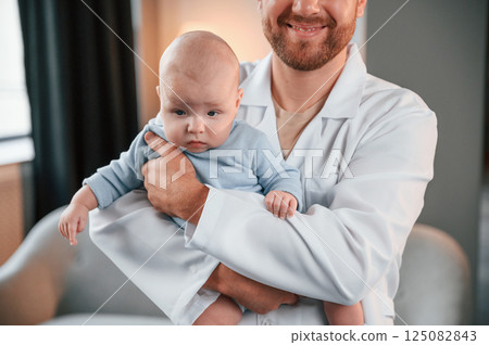 Doctor standing and holding newborn baby in hands indoors at apartment 125082843