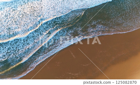 Top-Down Drone Shot of Waves Breaking on Smooth Sandy Shore Top-Down Drone Shot of Waves Breaking on Smooth Sandy Shore 125082870