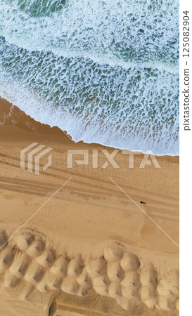 Aerial Drone Shot of Ocean Waves, Sand Mounds, and Beach Tracks 125082904