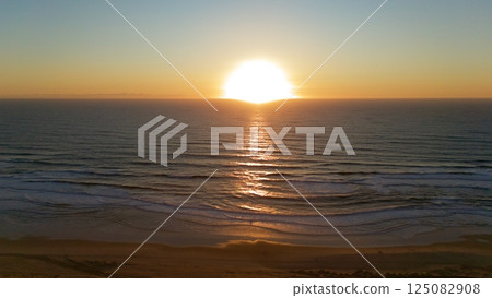 Golden Sunset Reflected on Ocean Waves and Sandy Beach 125082908
