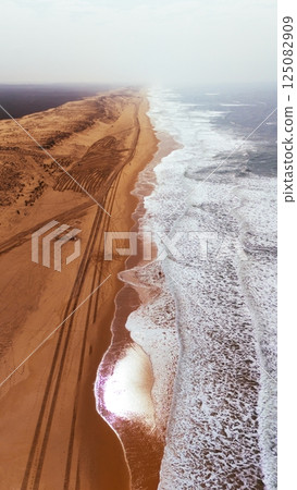 Aerial Drone View of Ocean Waves and Tire Tracks on Sandy Beach Aerial Drone View of Ocean Waves and Tire Tracks on Sandy Beach 125082909