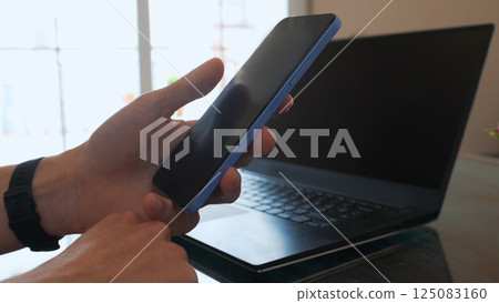 Person Using Smartphone and Laptop in a Bright Modern Workspace 125083160