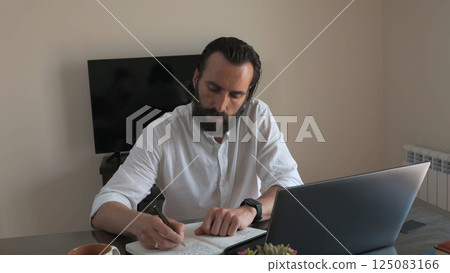Focused Man Working Diligently at Desk with Laptop and Notebook 125083166