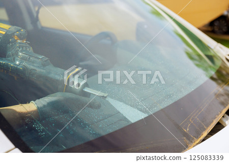 Worker uses power tool to repair car windshield in auto service station garage. Worker uses power tool to repair car windshield in auto service station garage. 125083339