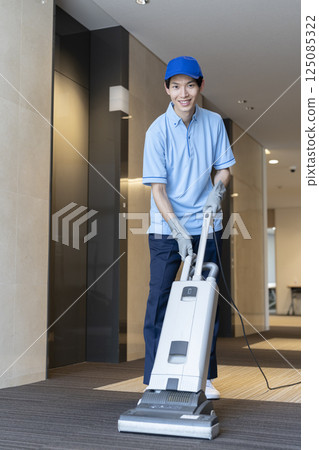 A young male cleaning staff working with a commercial carpet vacuum cleaner, looking at the camera 125085322