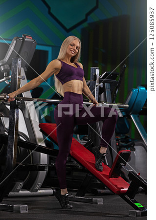 woman dressed in stylish purple activewear strikes a dynamic pose in a contemporary gym. She showcases her strength and fitness dedication against a backdrop of workout equipment and vibrant colors. woman dressed in stylish purple activewear strikes a dynamic pose in a contemporary gym. She showcases her strength and fitness dedication against a backdrop of workout equipment and vibrant colors. 125085937