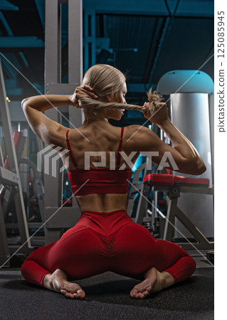 woman with a toned physique is engaged in a fitness routine at a contemporary gym. She stretches and poses to enhance her flexibility and strength. 125085945