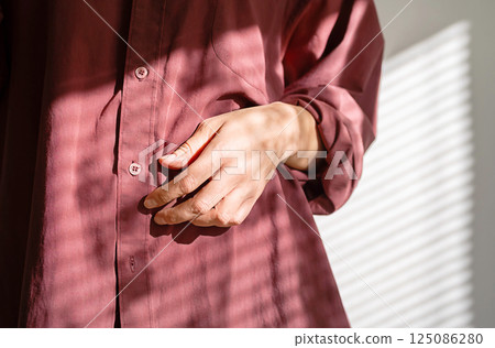 Females Hand Resting on Her Vintage Burgundy Shirt Dappled with Window Light. Fashion Design Blogs or Apparel Advertisements. 125086280