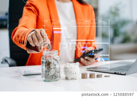businesswoman holding coins putting in glass with using smartphone and calculator to calculate concept saving money 125088597