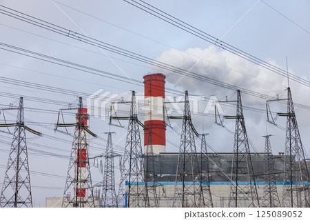 Large chimneys release white smoke in an industrial landscape filled with electricity pylons under a gray sky Large chimneys release white smoke in an industrial landscape filled with electricity pylons under a gray sky 125089052