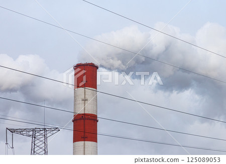 Emissions rise from a tall smokestack against a cloudy sky in an industrial area during early morning hours Emissions rise from a tall smokestack against a cloudy sky in an industrial area during early morning hours 125089053