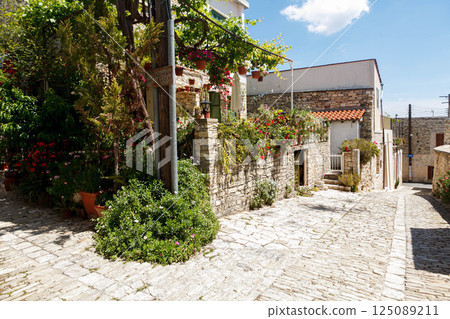 Charming cobblestone pathway adorned with vibrant flowers in Levkara, Cyprus during a sunny afternoon stroll 125089211